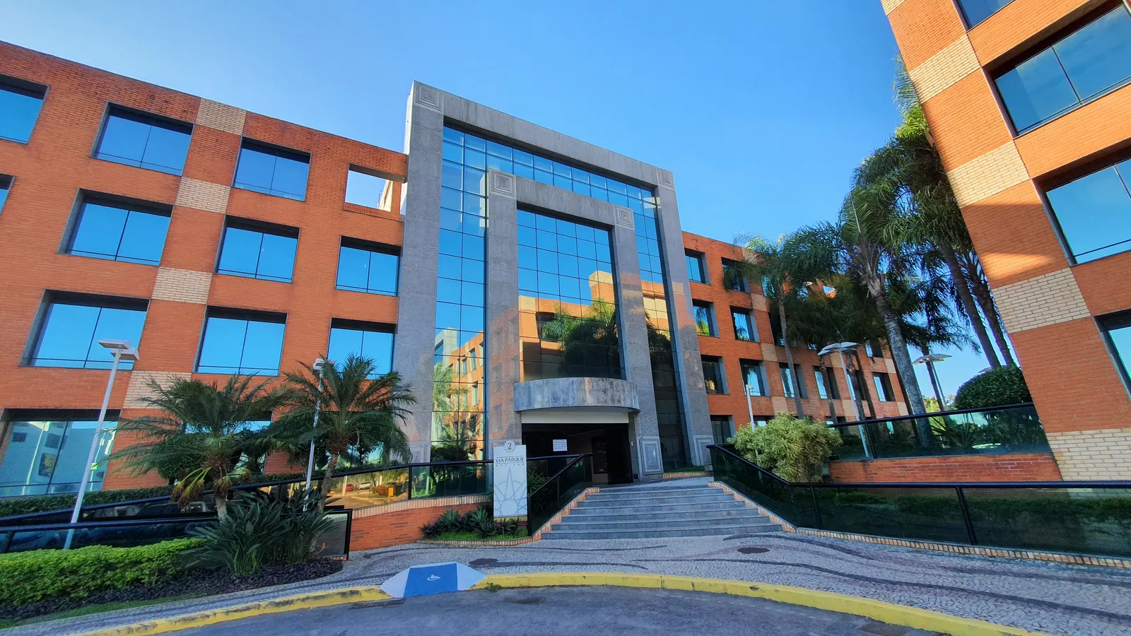 Entrada do Bloco 2 do Via Parque Offices, com escadaria e fachada de tijolos e vidro